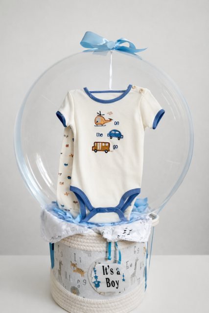 Globo transparente con ropita de bebé dentro, sobre una canasta “It's a boy”